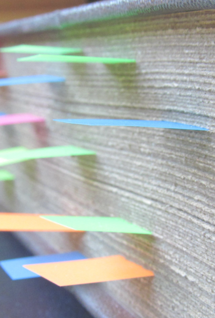 Billedet viser en tyk bog hvor man kan se en masse farverige post-its stikke ud af.